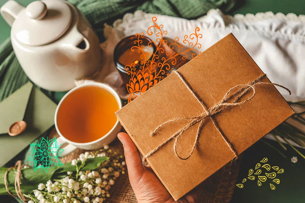Ręka trzyma prezent w brązowym pudełku przewiązanym sznurkiem, obok filiżanka herbaty i czajnik