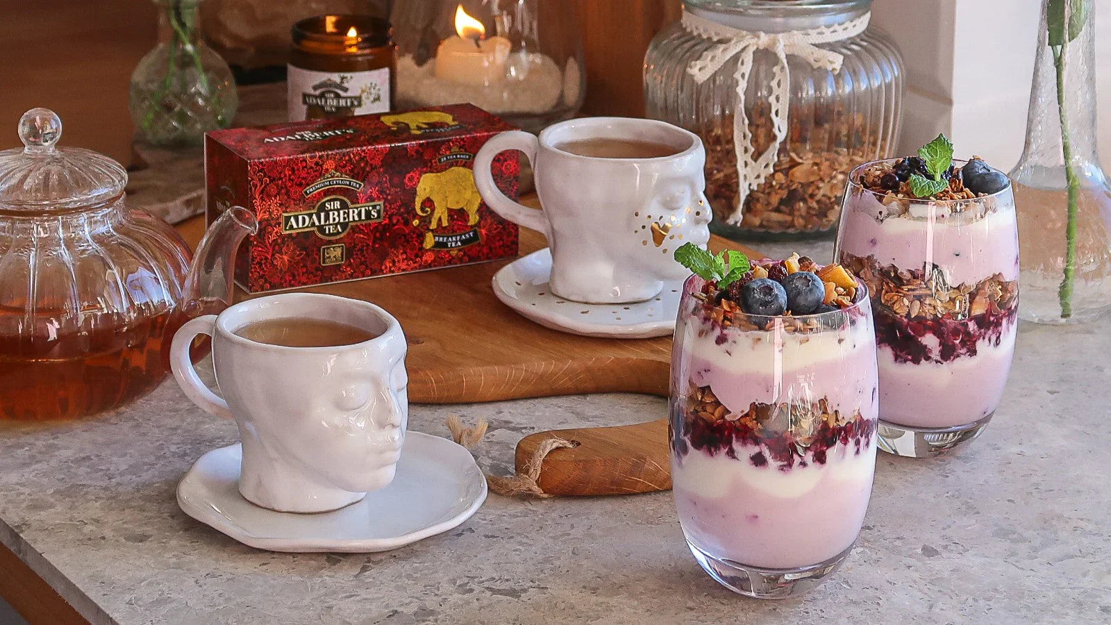 Śniadanie z herbatą Adalbert's, filiżankami z twarzami i deserami jogurtowymi z granolą i borówkami