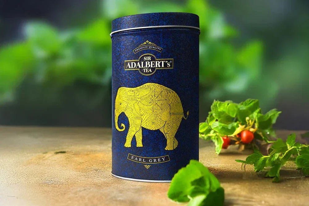 Puszka herbaty Sir Adalbert's Earl Grey z żółtym słoniem na ciemnoniebieskim tle z zielonymi liśćmi i owocami obok