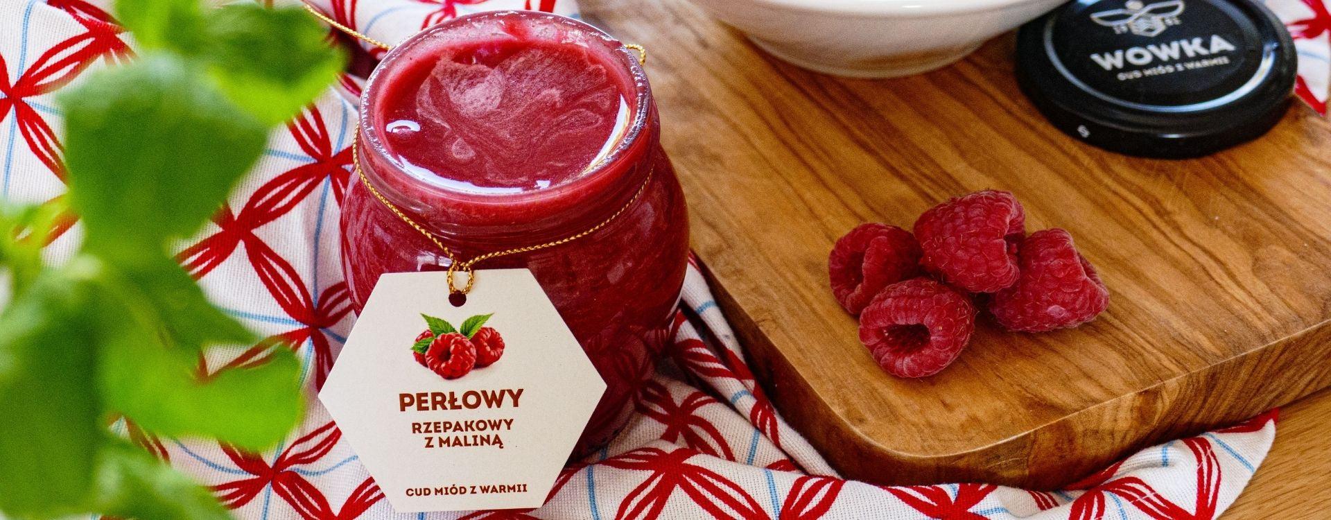 Słoik miodu rzepakowego z maliną Perłowy z etykietą obok świeże maliny na desce drewnianej