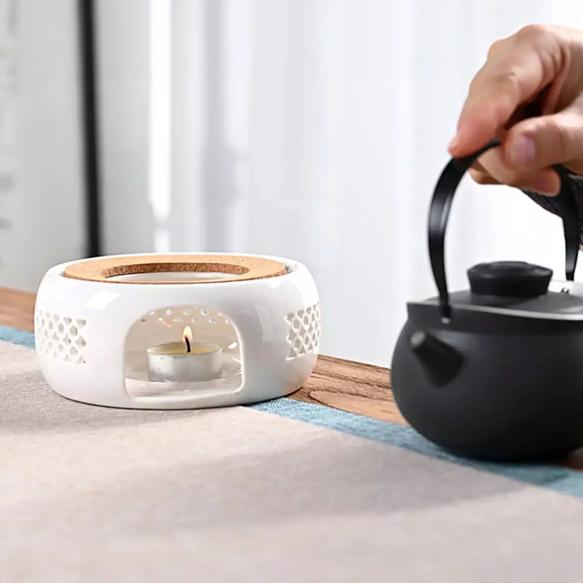 Biały ceramiczny podgrzewacz z tealight i czarny czajnik na drewnianym stole