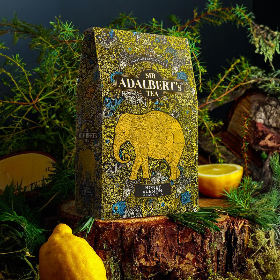 Opakowanie herbaty Sir Adalbert's Honey & Lemon czarna herbata na tle drewna, cytryny i zielonych gałązek