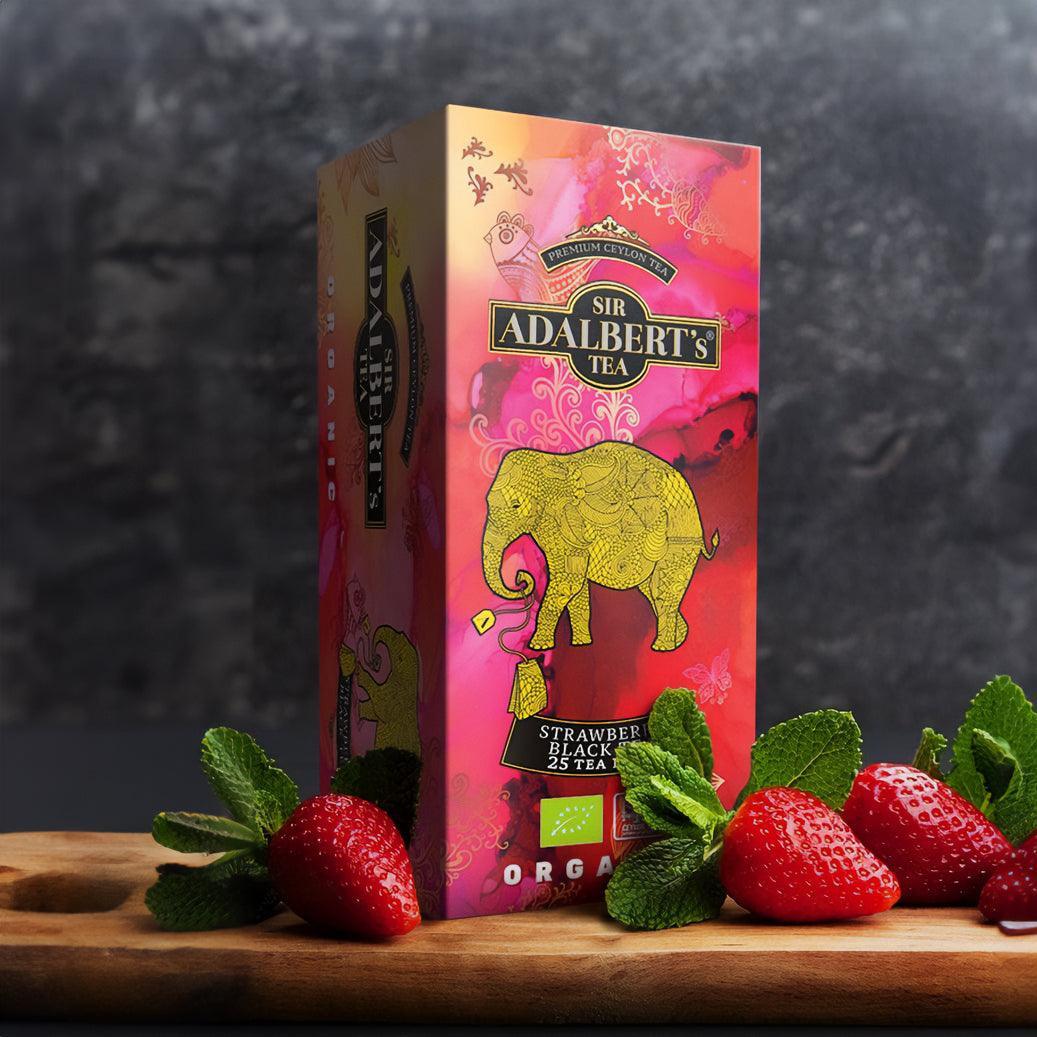 Opakowanie herbaty Sir Adalbert's Strawberry Black Tea organiczne z ilustracją słonia i świeże truskawki z miętą na drewnianej desce