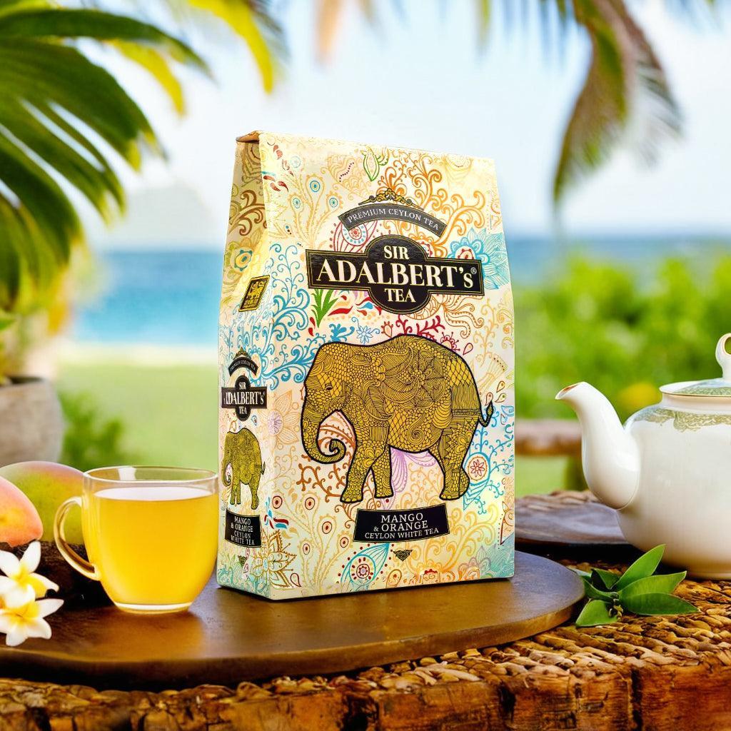 Opakowanie herbaty Sir Adalbert's Tea Mango & Orange biała herbata Ceylon na drewnianej tacy z filiżanką i dzbankiem, tropikalne tło