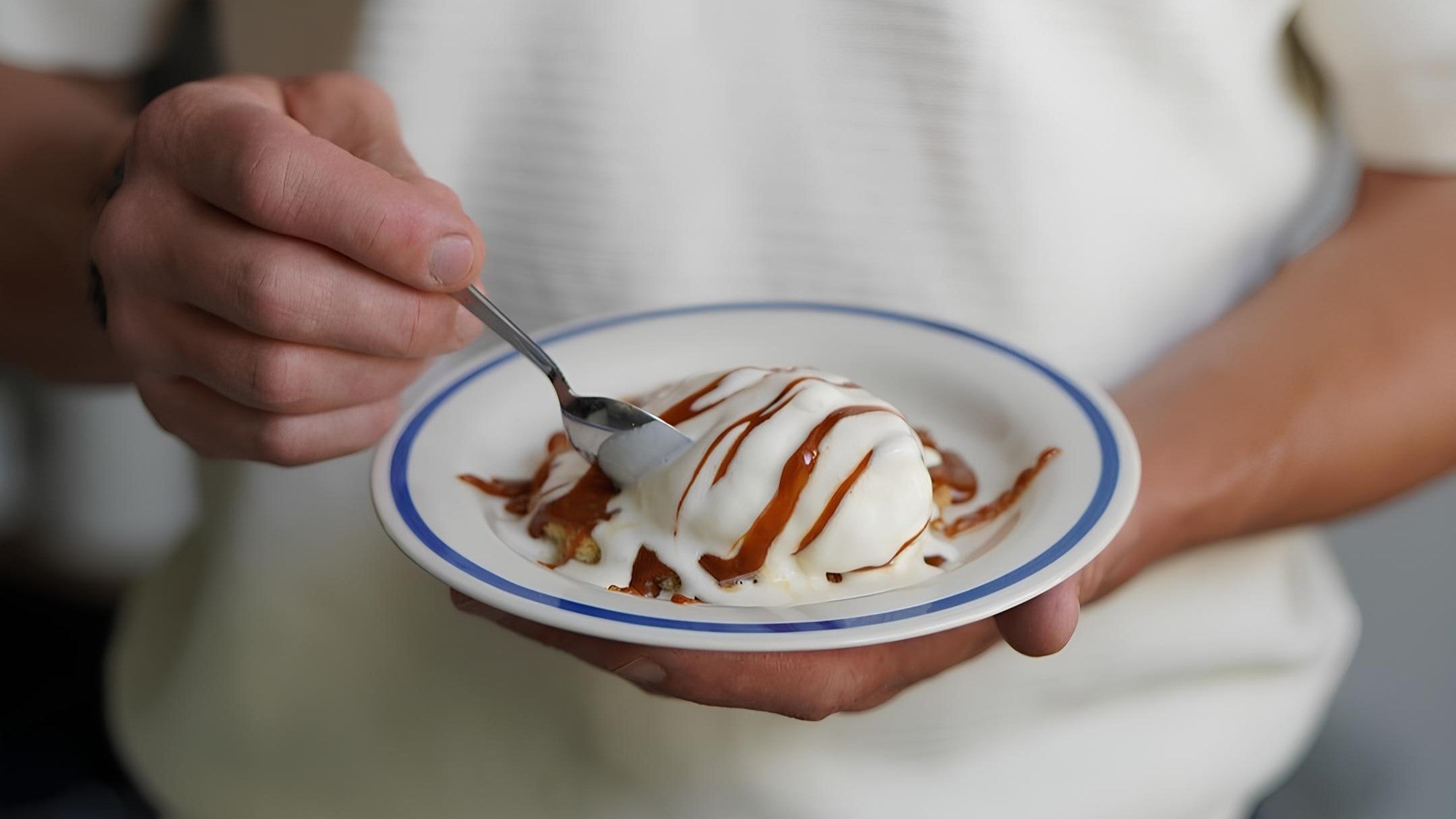 Ręka trzyma talerz z deserem lodowym polanym czekoladą i łyżka