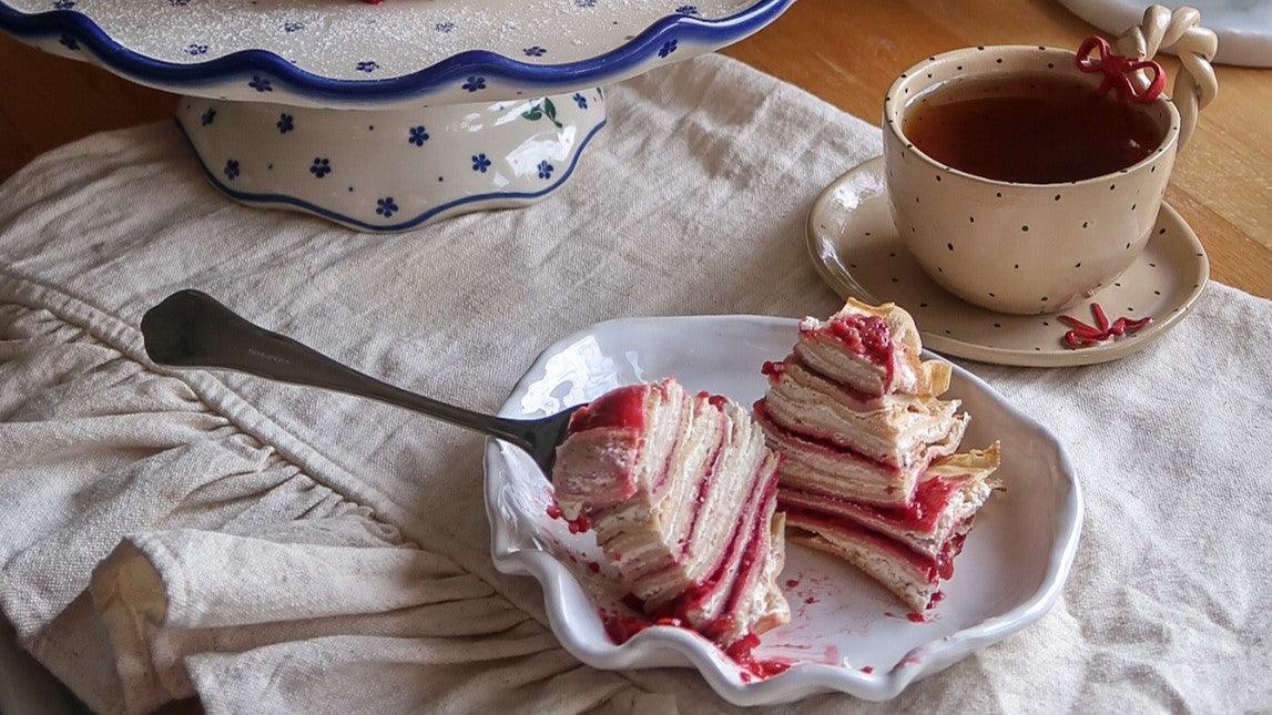 Porcelanowy talerzyk z ciastem warstwowym z malinowym nadzieniem i filiżanka herbaty na lnianym obrusie