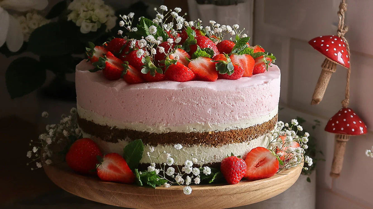 Tort truskawkowy z kremowymi warstwami, świeżymi truskawkami i kwiatami dekoracyjnymi na drewnianej podstawce
